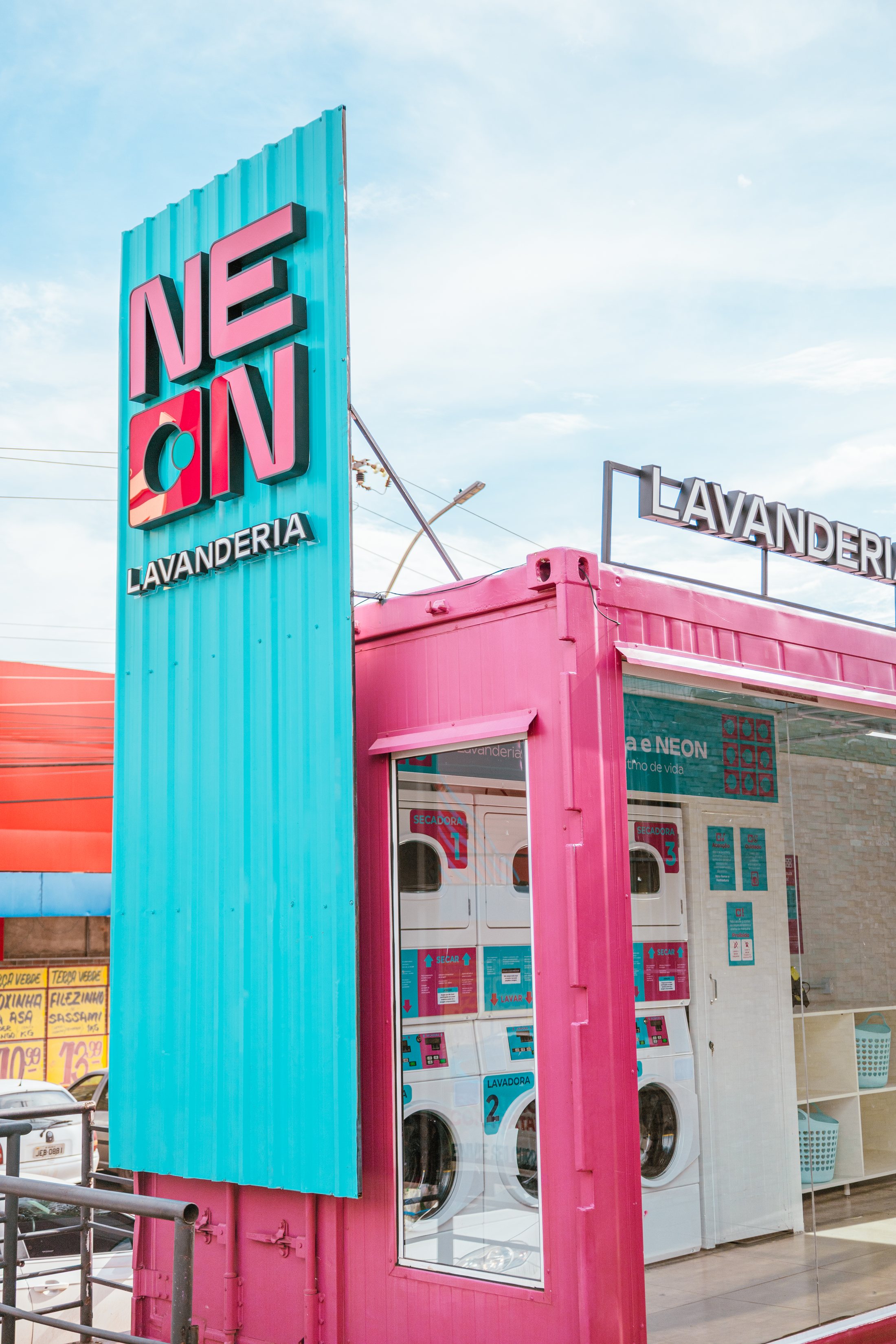 Fachada da Neon Lavanderia, container rosa e turquesa com máquinas de lavar visíveis através do vidro